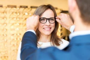 optometrist helping woman try on new eye glasses