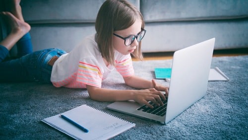 young girl wearing glasses while doing homework on computer